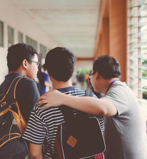 Group of male teenagers walking in a school corridor with backpacks, bonding and chatting.