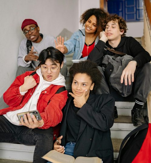A diverse group of students posing together on stairs, taking a selfie indoors.