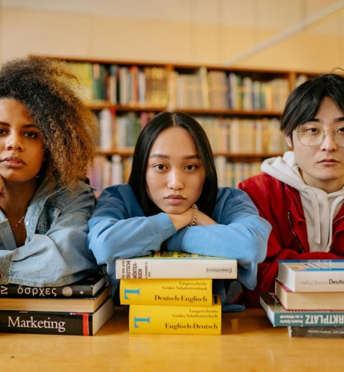 A group of diverse students engaging in studies at a library, surrounded by books and resources.